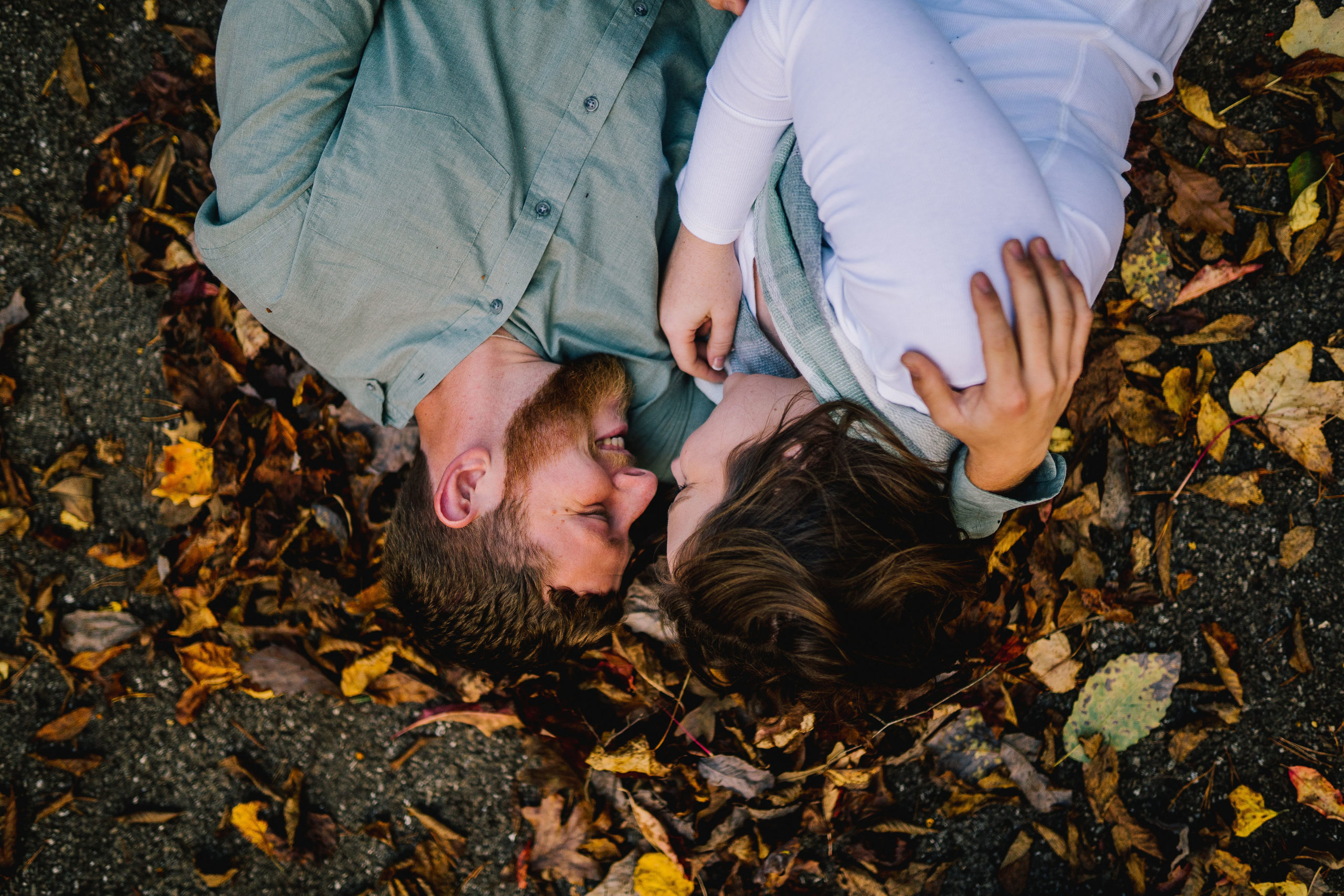 husband and wife during an engagement session laying on fall leaves holding each other at Norris Lake
