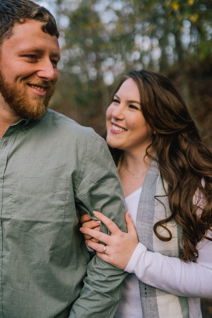 woman holding a mans arm and smiling at each other at Norris Lake in the fall for an engagement session