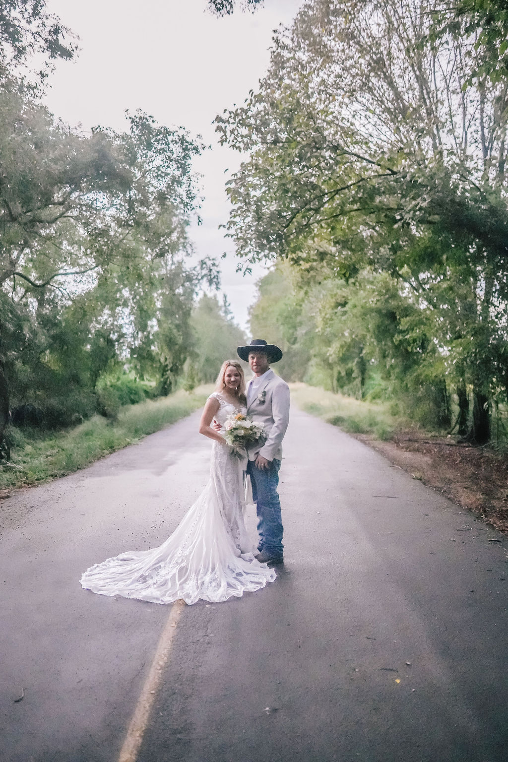 bride and groom standing in the road under an arch of trees