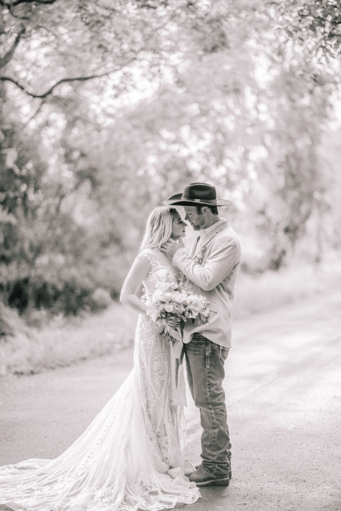 black and white photo of a Louisiana couple on their wedding day. Southern groom holding his brides cheek as she holds her bouquet. Grooms in cowboy hats