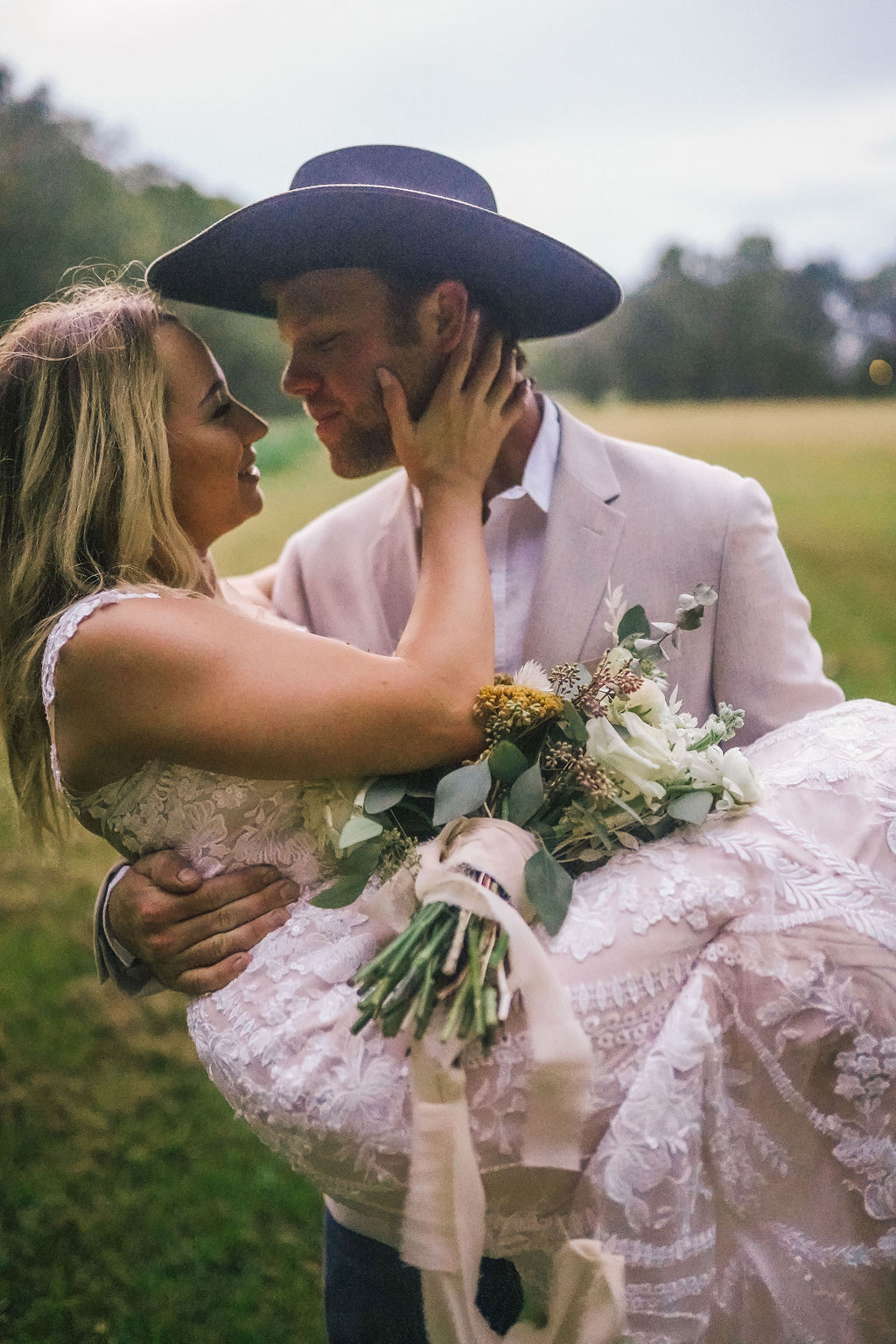 Groom carrying his bride into the field. Southern groom in cowboy hat. Elegant Louisiana bride.