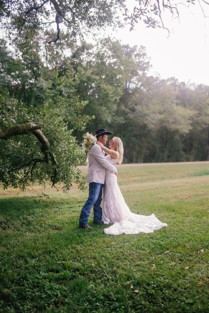 Bride and groom embracing each othe rin Louisiana on their wedding day. Groom in a cowboy hat and bride in a lace gown.