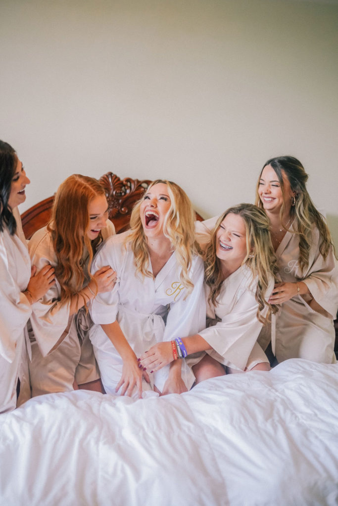 Bride and her bridesmaids laughing as they get ready in matching robes