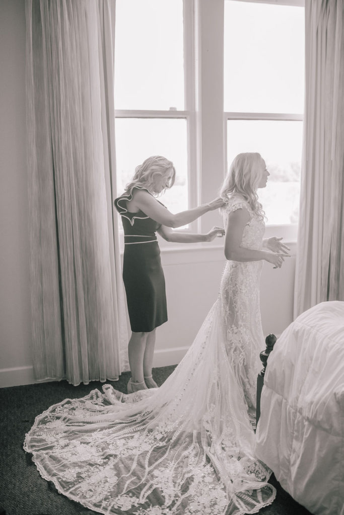 mother helping her daughter get dressed for her wedding day. Mom buttoning the brides dress in front of a wedding.