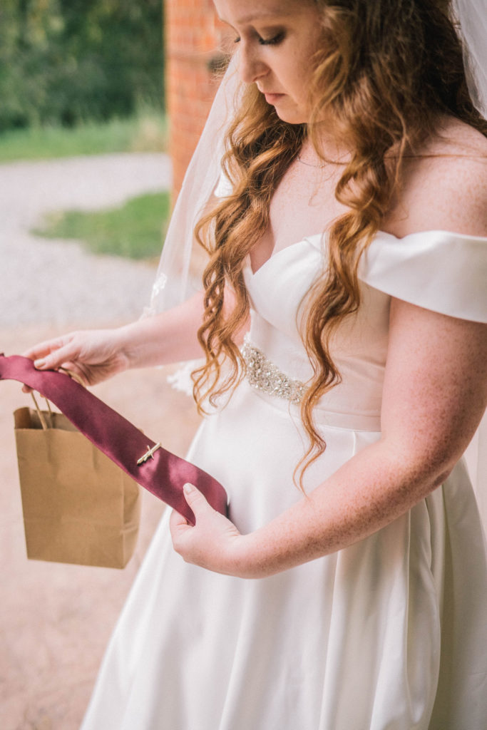 bride holding a red tie and tie clip for her father on her wedding day
