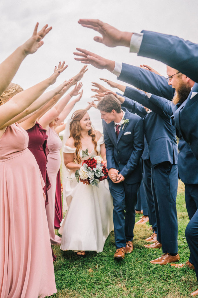 bride and groom holding hands and walking under the bridal party's hands that are reach up to form a tunnel