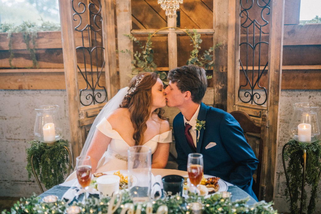 husband and wife on their wedding day at Butler Farms kissing at their reception in an old barn elegantly decorated