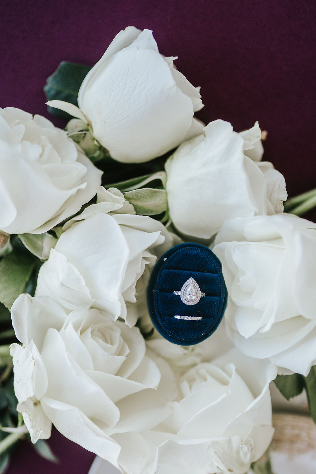wedding ring and engagement ring in a royal blue velvet box sitting on top of white roses for a wedding flatlay photo
