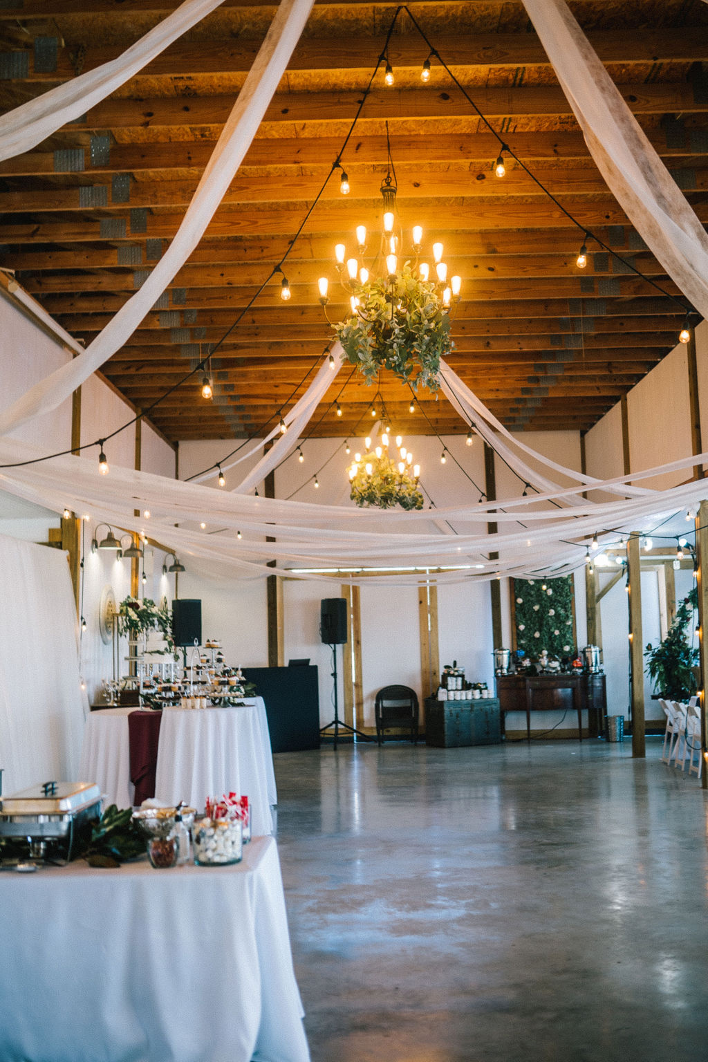 beautiful barn wedding venue in Knoxville Tennessee with wooden ceiling and chandeliers decorated with draped fabric and Edison bulb strings of lights