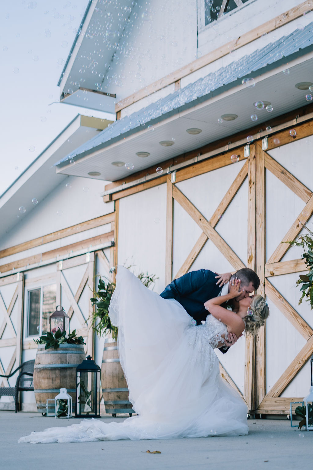 Bride and groom leaning over for a kiss in front of their barn venue