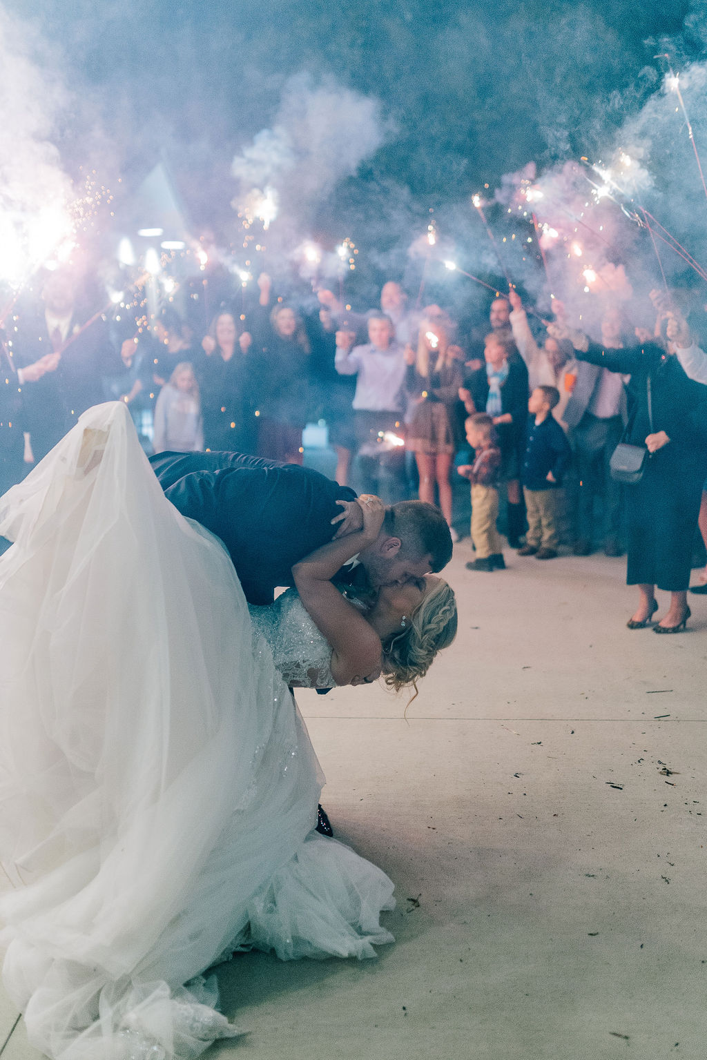 groom dipping his bride really low as he kisses her and the guests send them off with sparklers