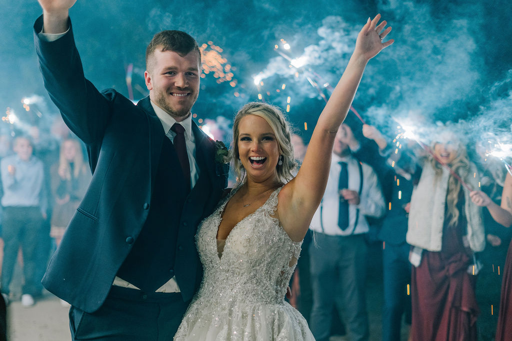 bride and groom send off for their destination wedding with sparklers and blue lights surrounding them as they smile at the camera with their hands in the air