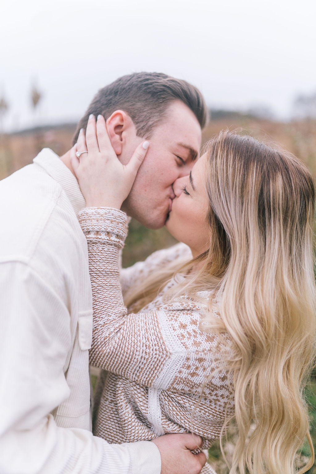 man and woman kissing in a golden meadow in Knoxville for their engagement session in the winter with winter engagement session outfits