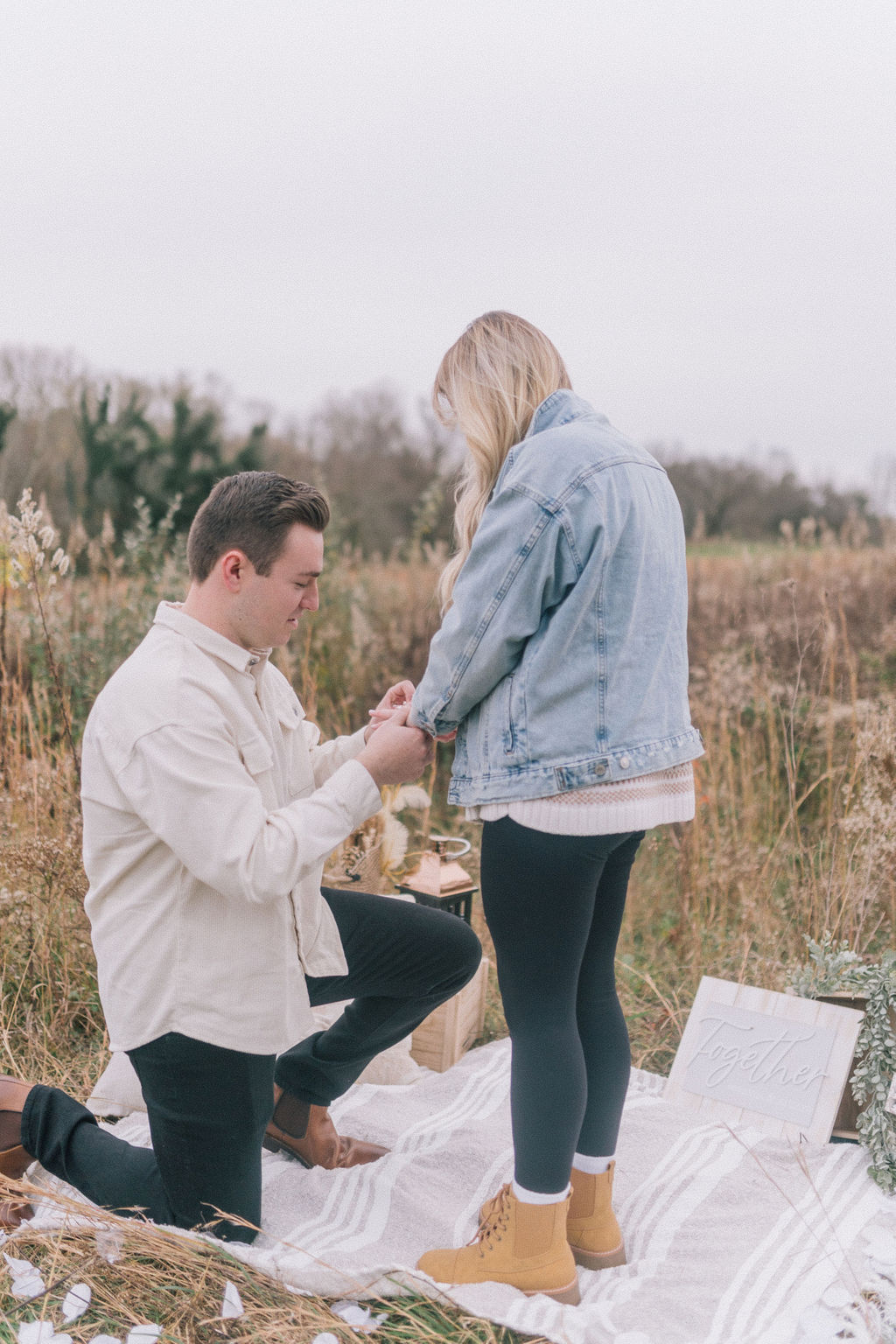 man and woman getting engaged in knoxville field on blanket during surprise proposal