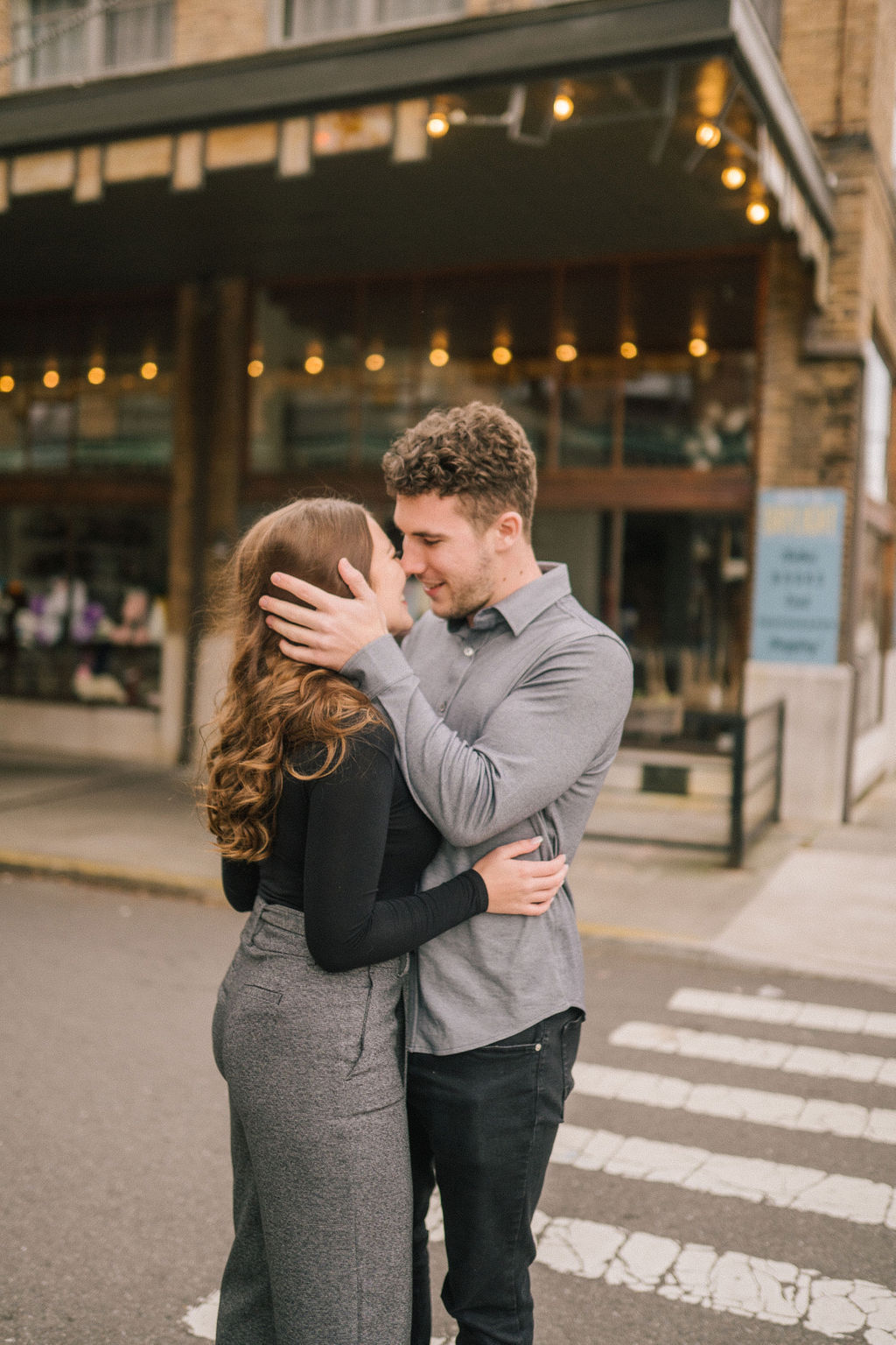 winter engagement outfits inspiration in Knoxville Tennessee with the best Knoxville wedding photographers with man and woman standing in the streets on downtown Knoxville with the man holding the womans head and the woman holding the mans waist as they both smile and laugh