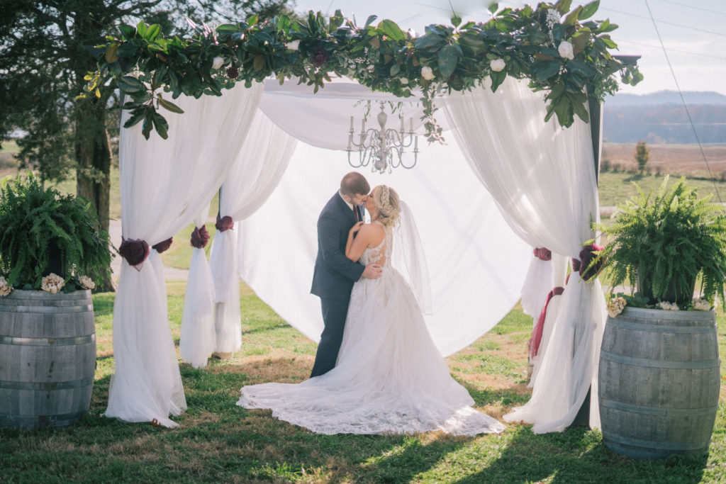 classy bride and groom kissing under the draping of an arch at their wedding ceremony