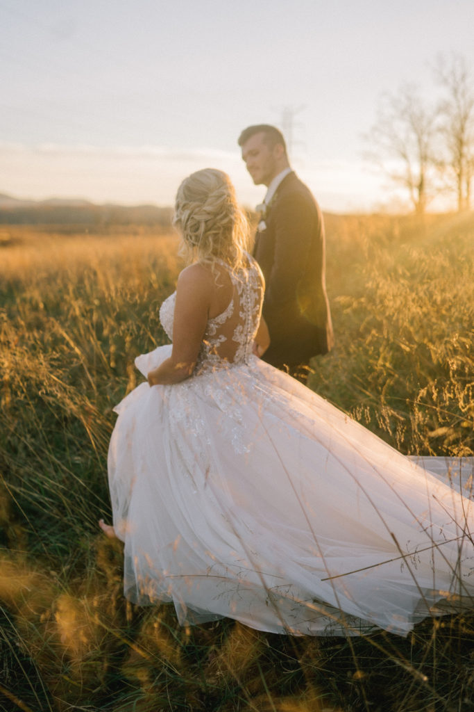 bride and groom walking through a Tennessee field on their wedding day. White laced ballgown