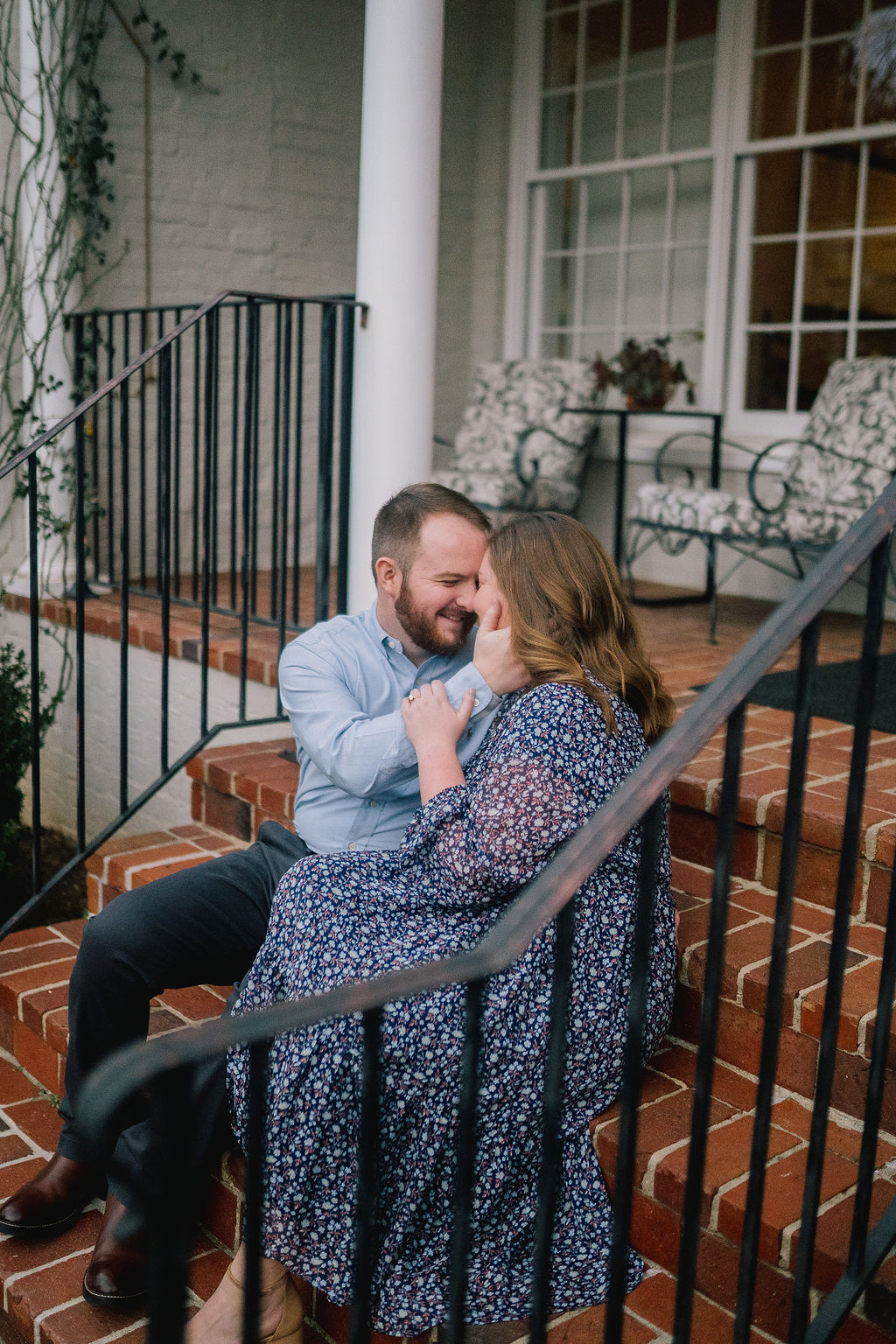 engagement session on a front porch in Knoxville Tennessee. Man holding woman's face. woman wearing navy blue summer dress for her engagement session
