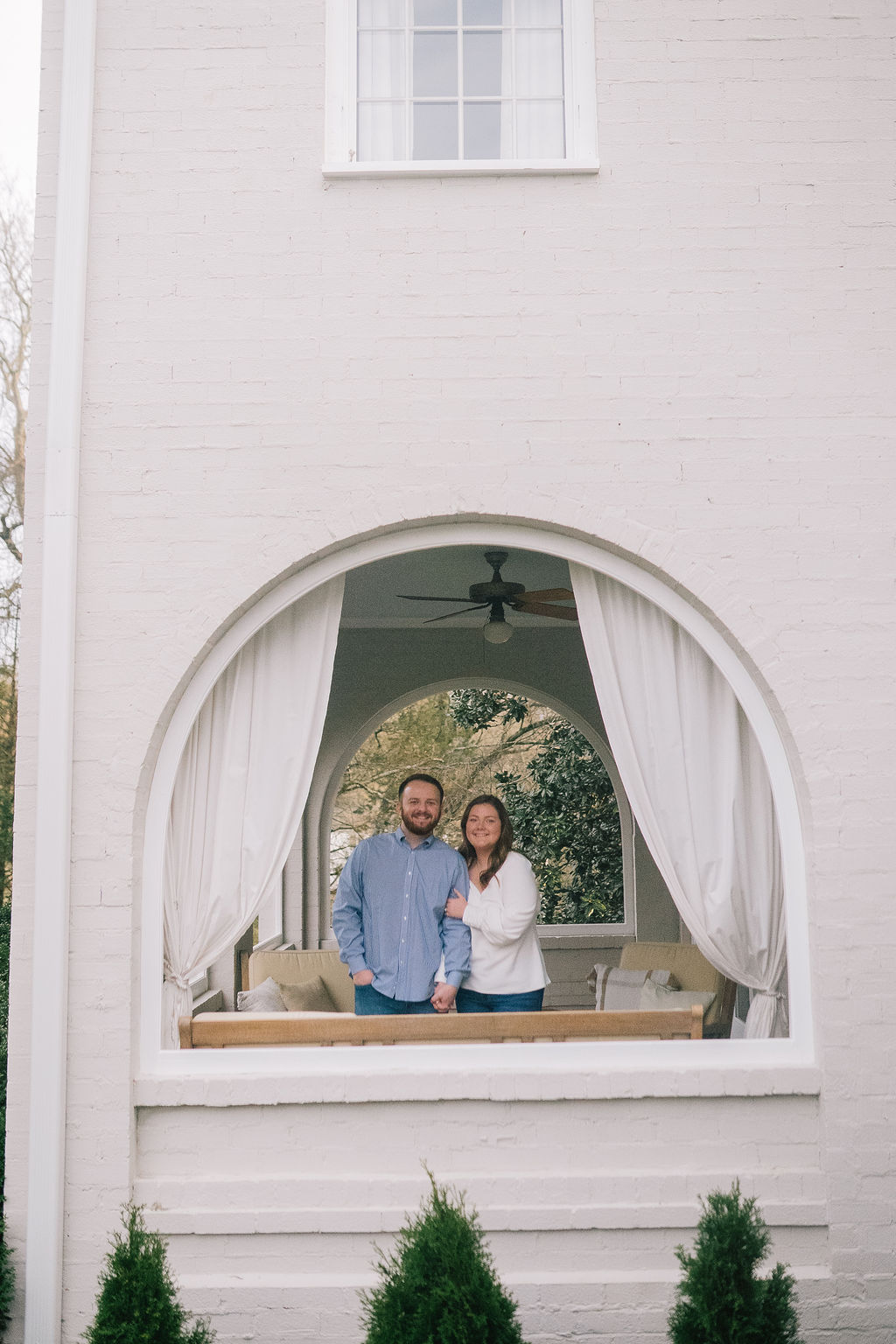 arched window with engaged couple standing inside