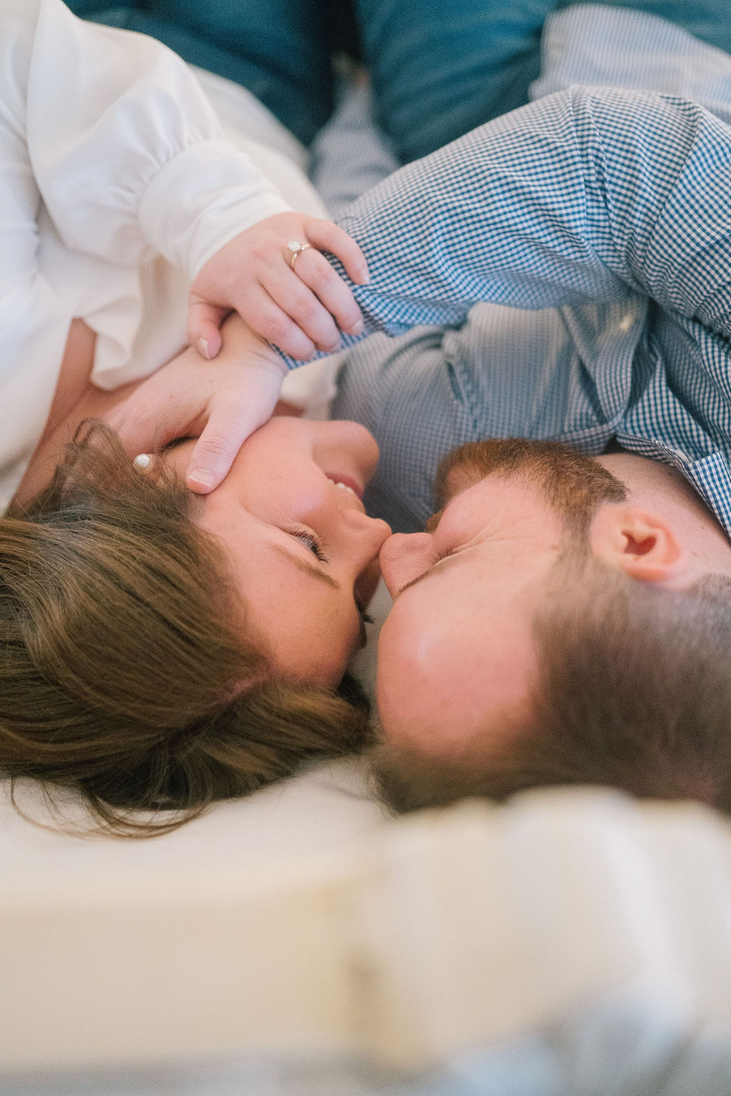 in home engagement session with the couple laying on the bed holding each others faces