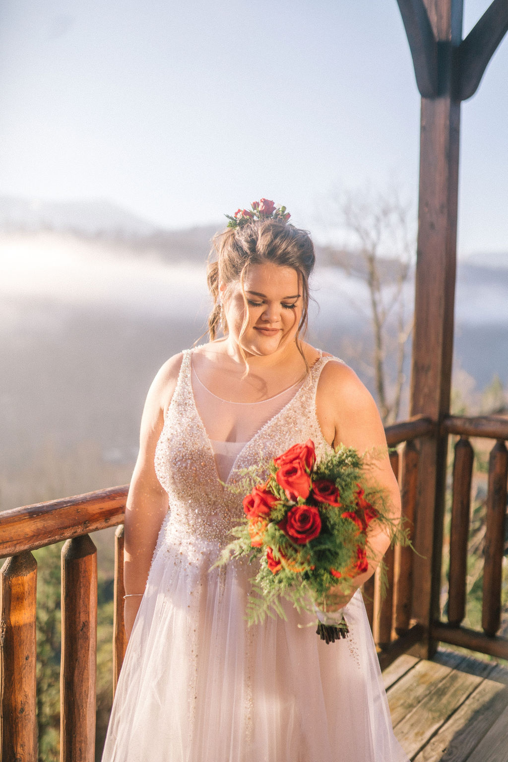 smoky mountain bride on her wedding day holding a red rose bouquet as the sunshine comes in through the clouds