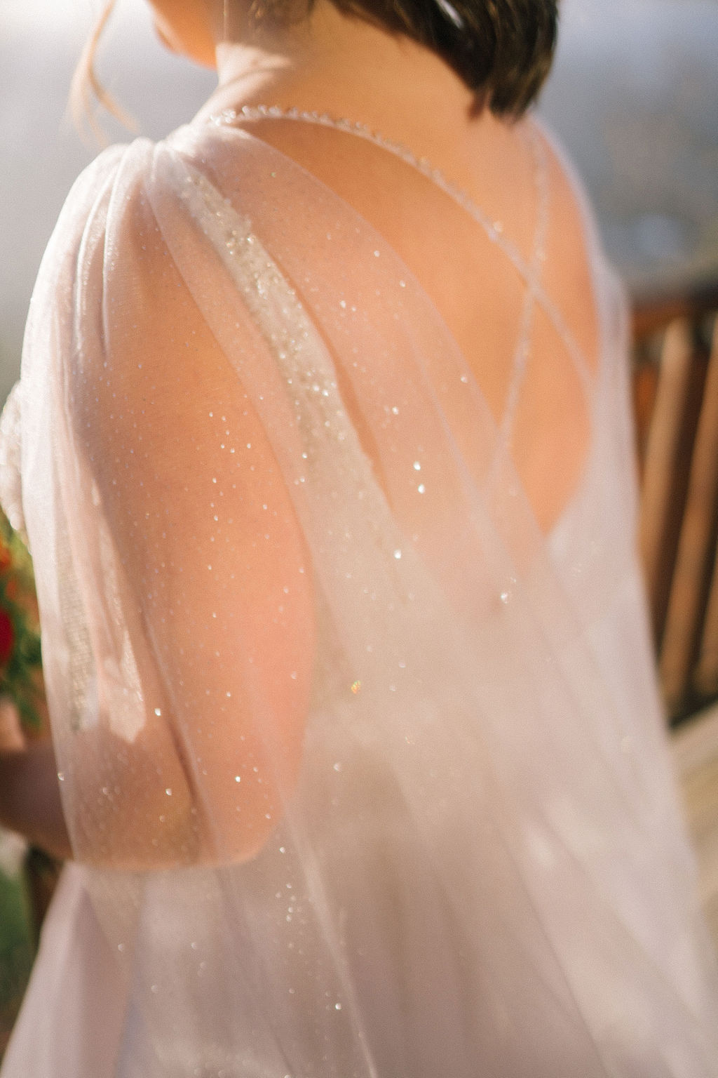 deatil shot of the brides dress with an open back and a long elegant cape that sparkles in the sun