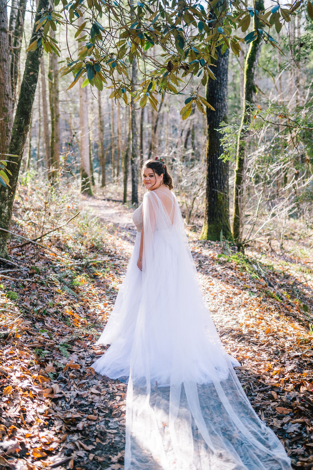 gorgeous forest bride with a long cape trailing behind her as she looks back at the camer. smoy mountain elopement photorgapher