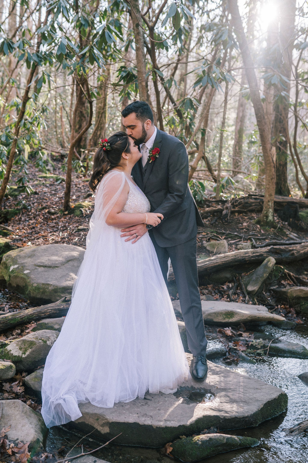 groom kissing his bride on the forehead as they standin gin a stream on their wedding day in smokies.