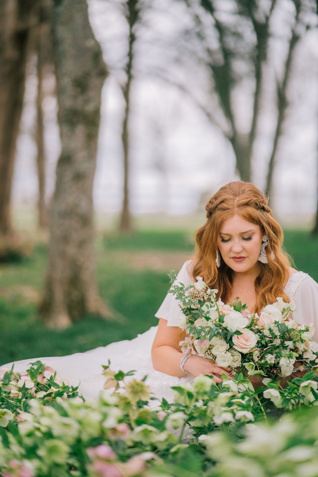 bride sitting a field of flowers holding her florals. Elegant and beautiful redheaded bride