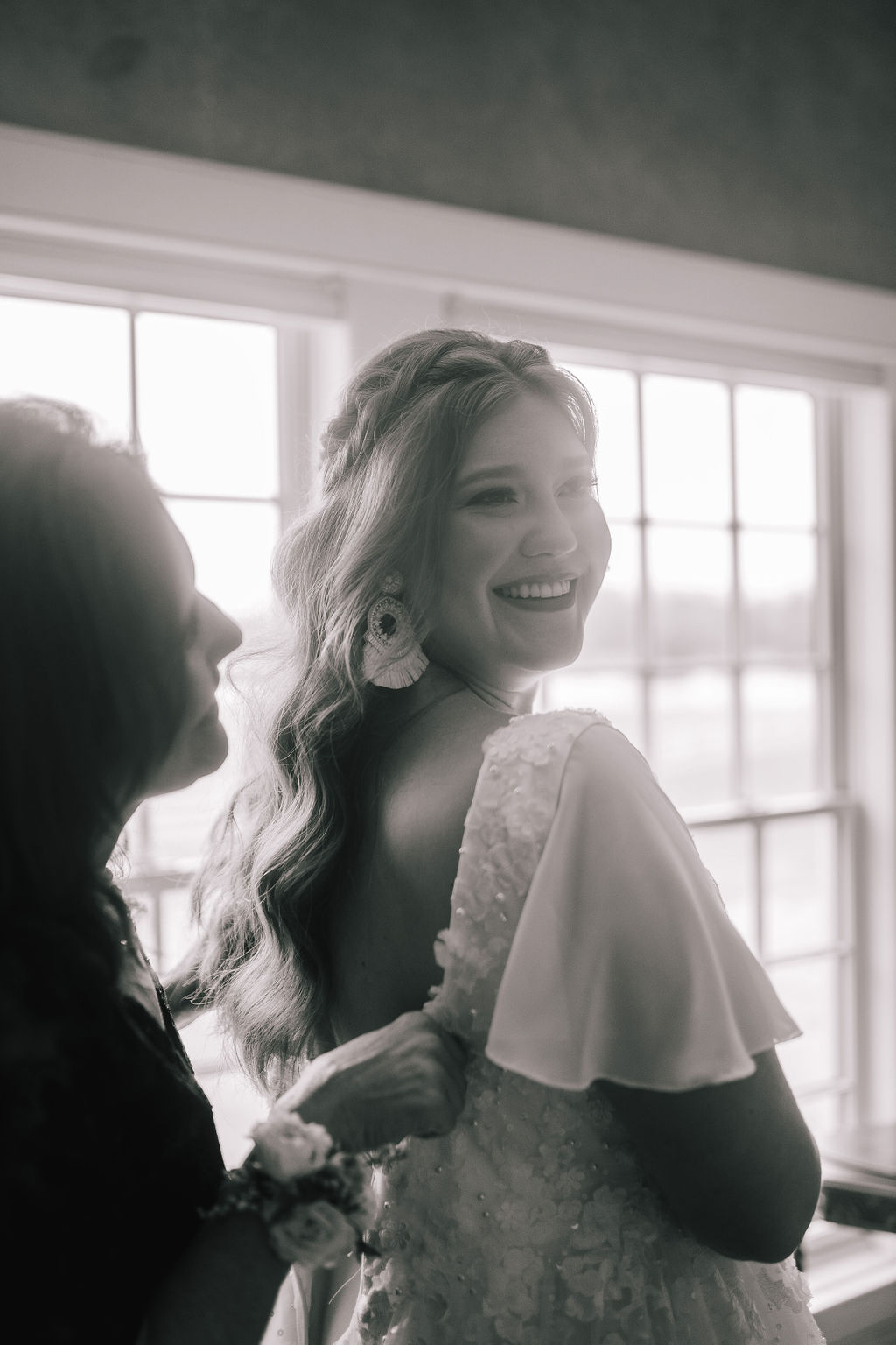 black and white photo of the bride in front of a window at the Marblegate Farm in Tennessee with her mom buttoning up her dress back for a special moment