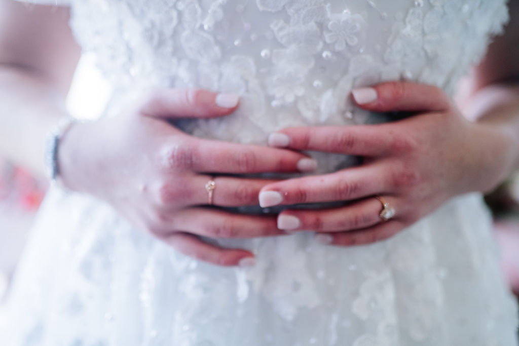 bride holding her torso to show her wedding day jewlery and the details of her dress