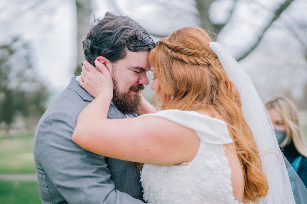 red head bride holding her grooms face as they smile on their Spring wedding at Marblegate Farm