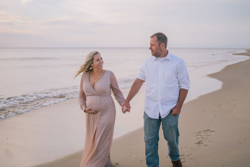 husband and wife walking on the beach at the Outerbanks in North Carolina for their maternity session at sunrise