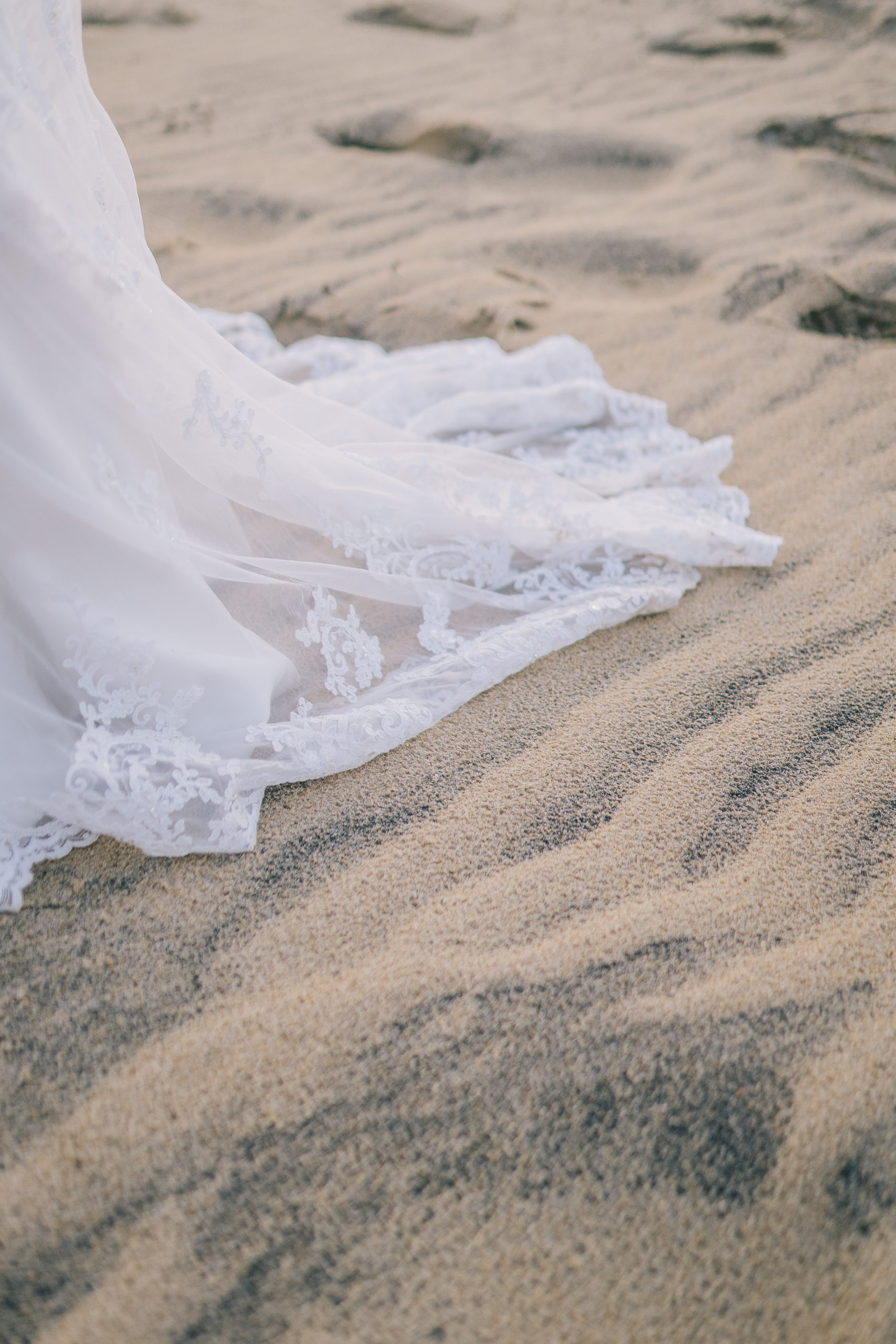 brides lace train across the sand as she walks.