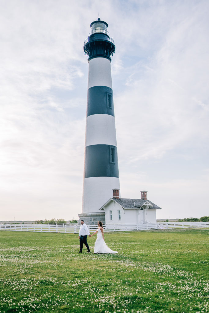 bride and groom walking infront of a black and white striped lighthose during their lighthouse adventure session