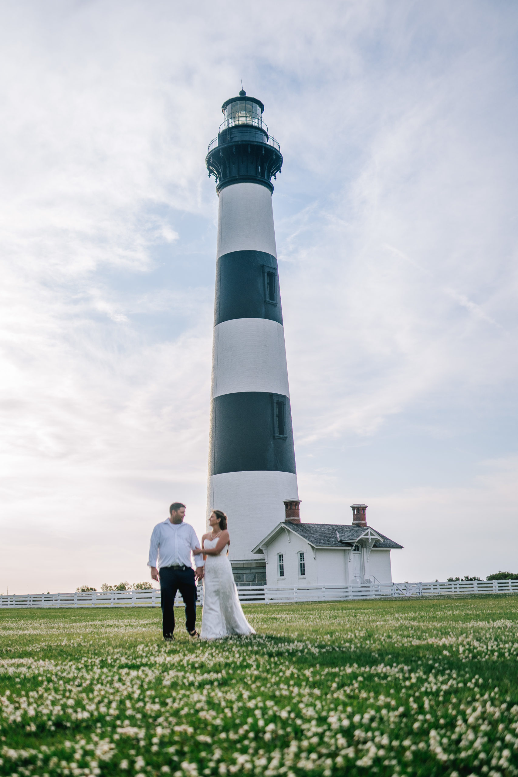 east coast bride and groom walking towards the camera with a black and white lighthouse behind them