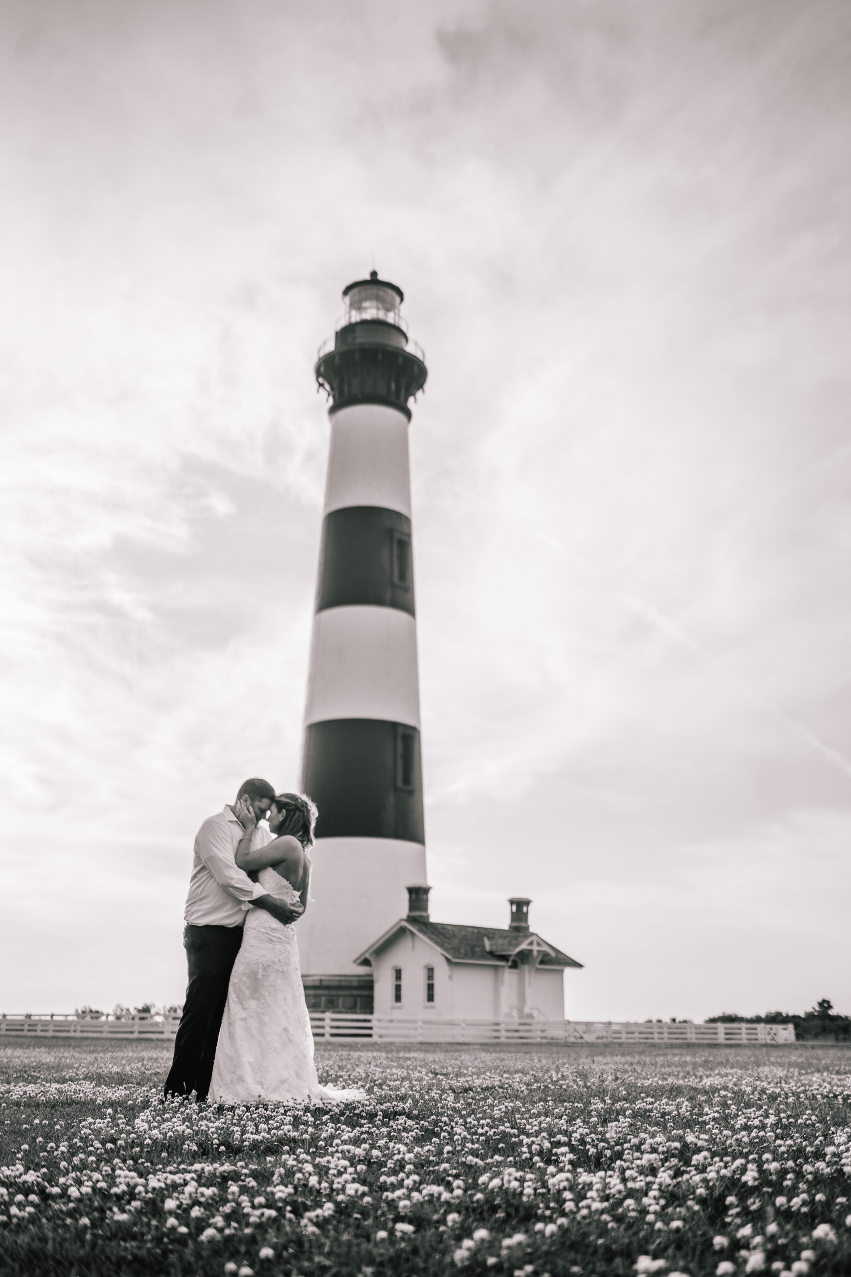 black and white photo of a bride and groom in front of a lighthouse on the east coast taking their bridal photos.