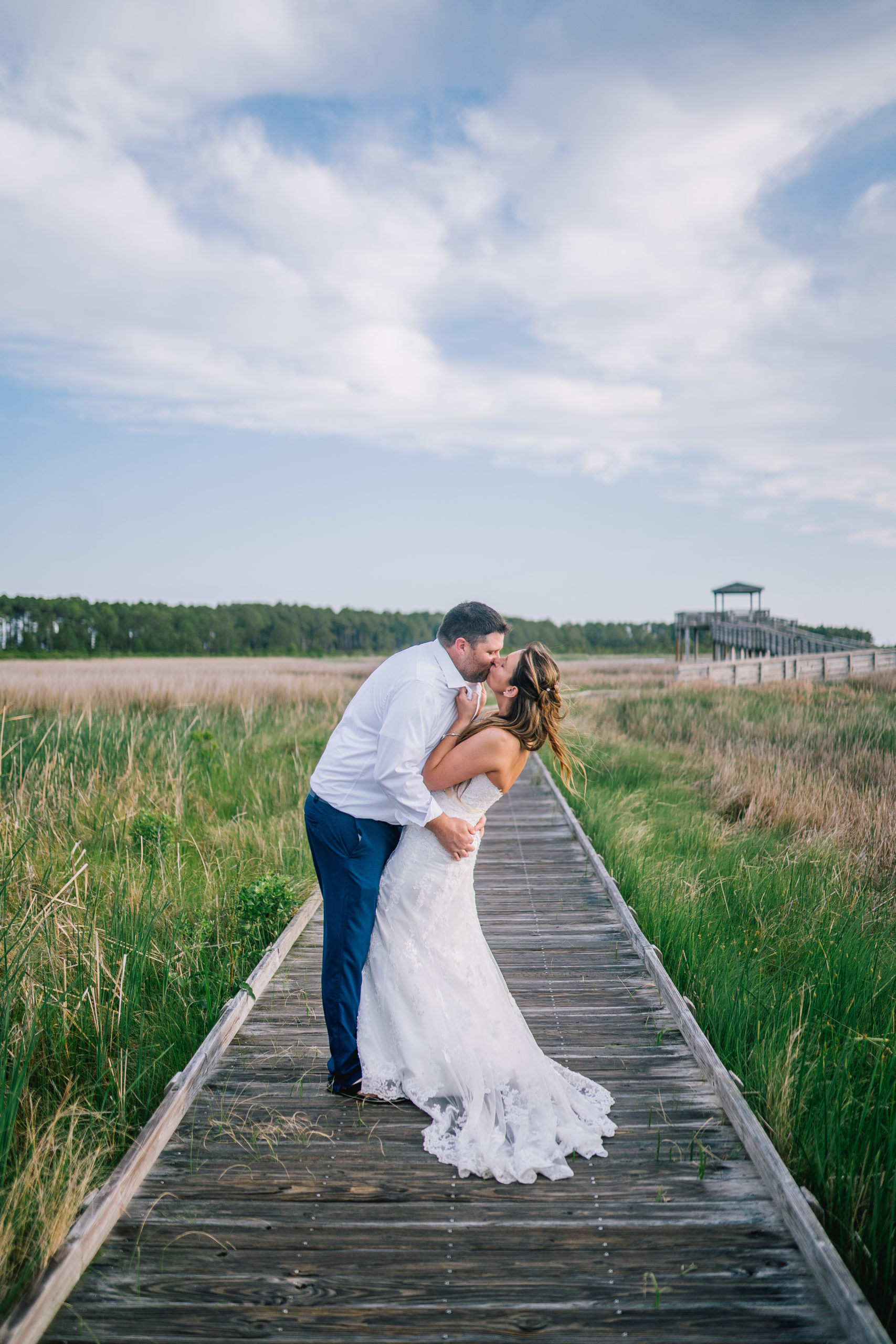 eastcoast bride and groom kissing on a boardwalk next to their beach wedding in the spring