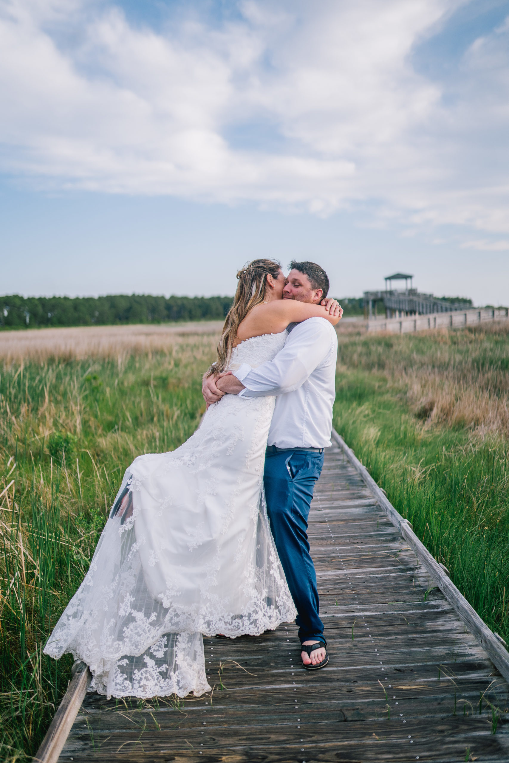groom picking up bride on a boardwalk and spinning her around as her lace train flows through the air