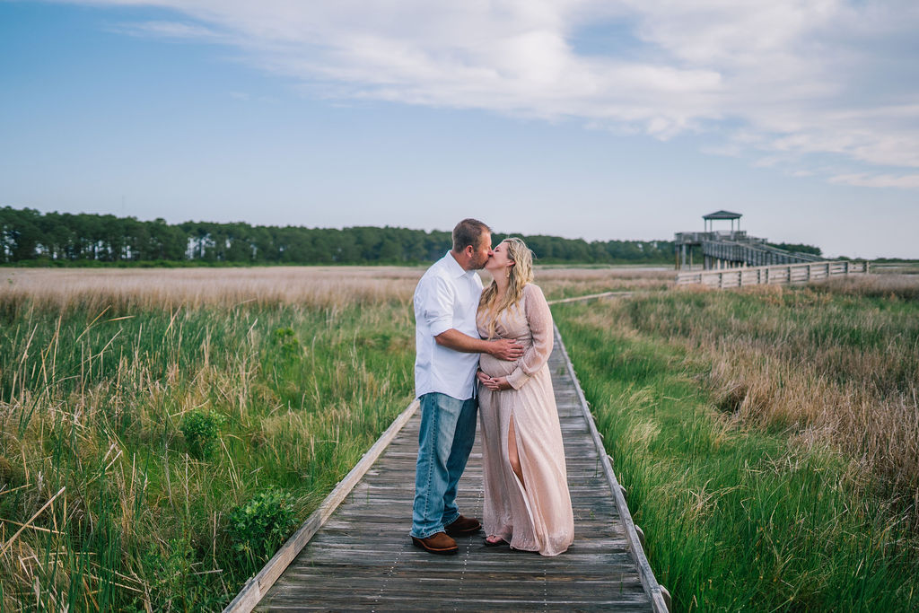 man and woman kissing on a dock for their maternity session in North Carolina. Man is holding the womans baby bump