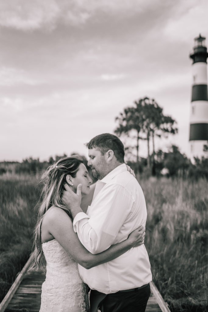 black and white photo of a groom holding his brides face and kissing her forehead during their lighthouse adventure session
