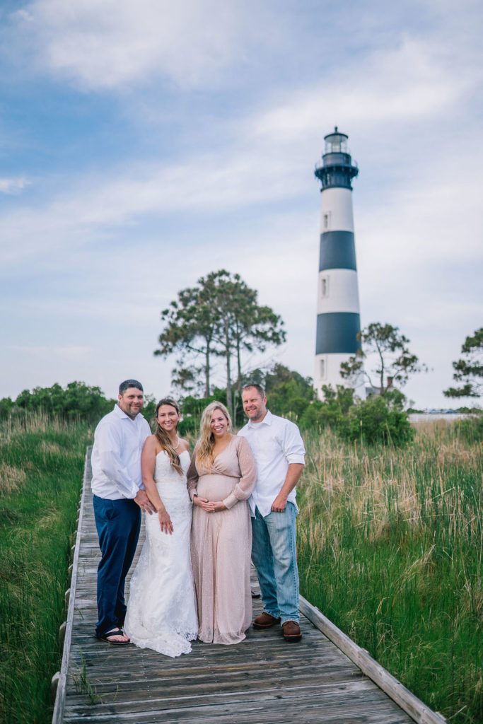 bride and groom with best friends on the Outerbanks walking on a dock near a black and white lighthouse