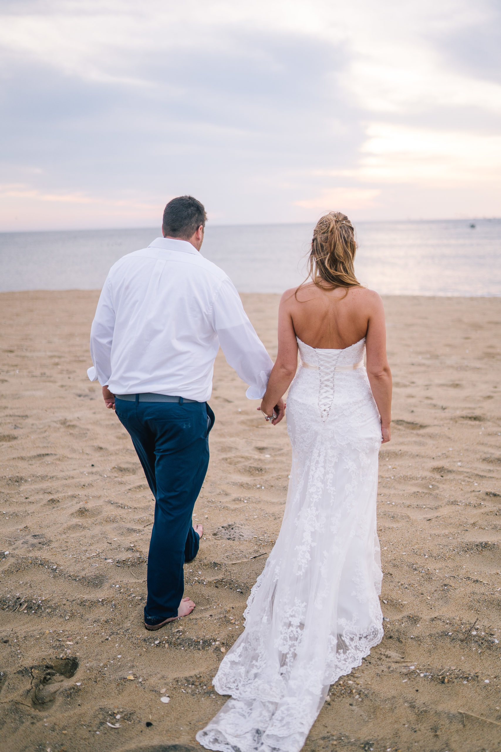 lighthouse adventure session with the bride and groom on the beach walking away from the camera at sunrise