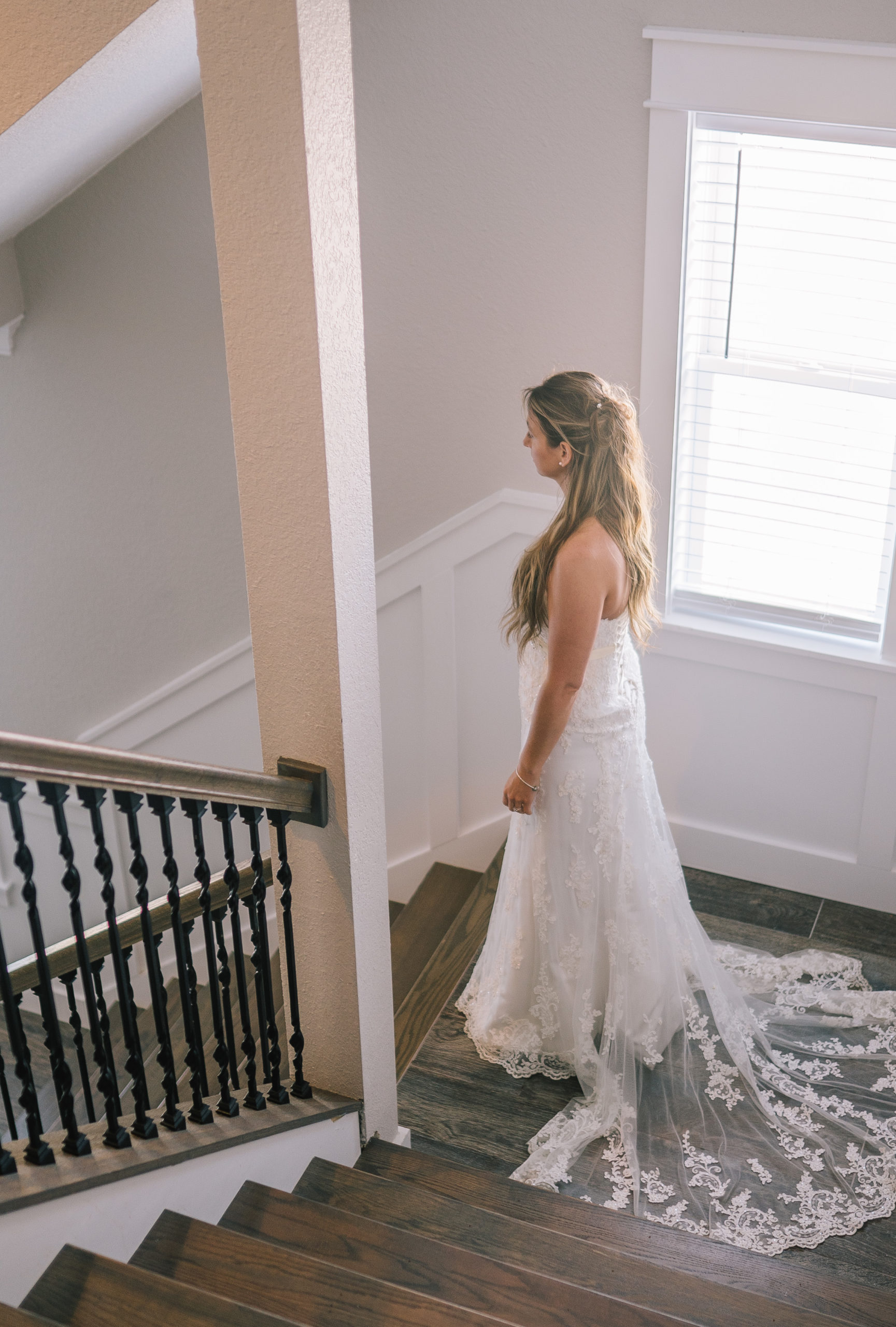 bride standing on a stairwell in her lace wedding dress next to a window