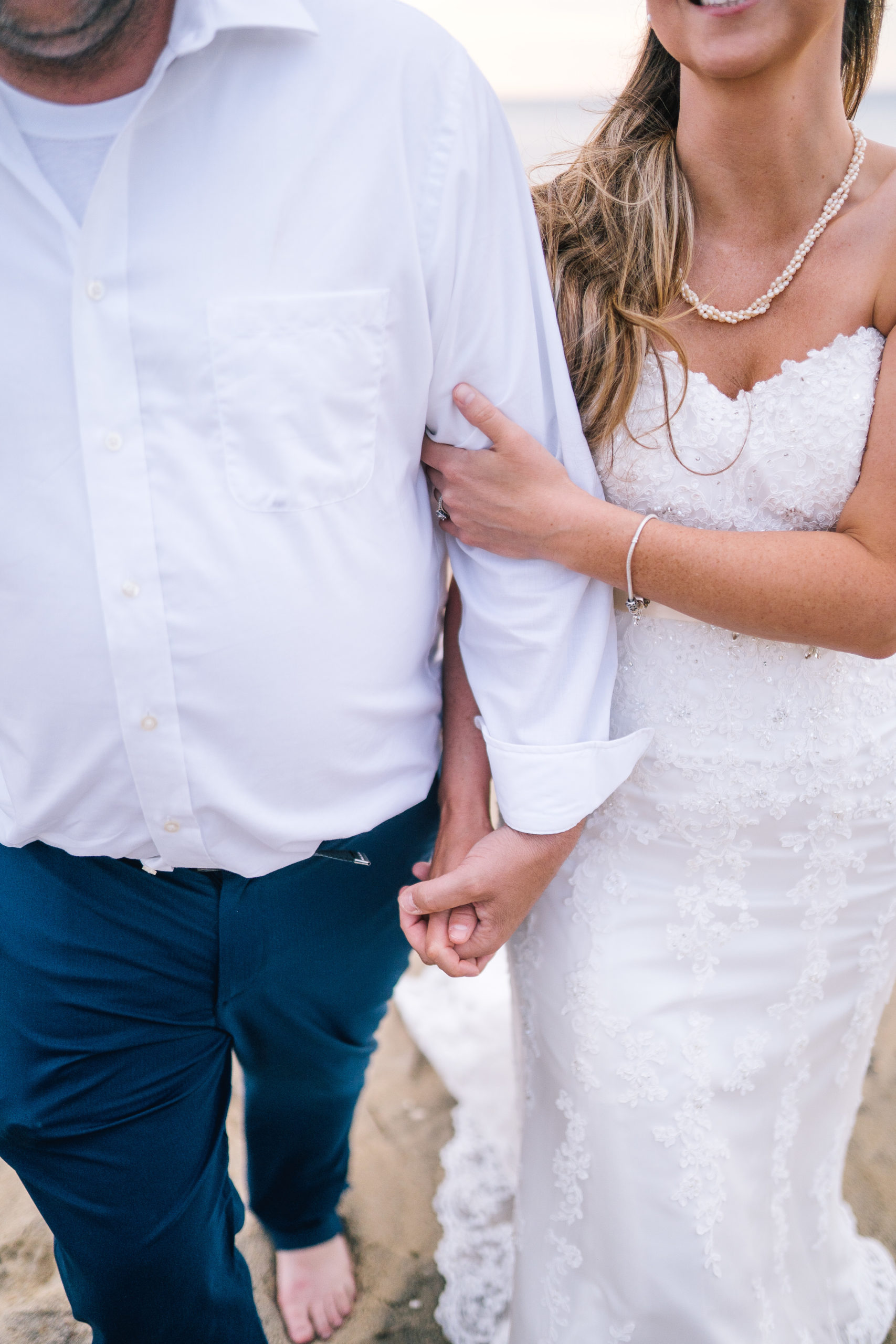 detail shot of the brides dress. lace bridal gown with a sweetheart neckline. Bride and groom holding hands on the beach. Lighthouse adventure session