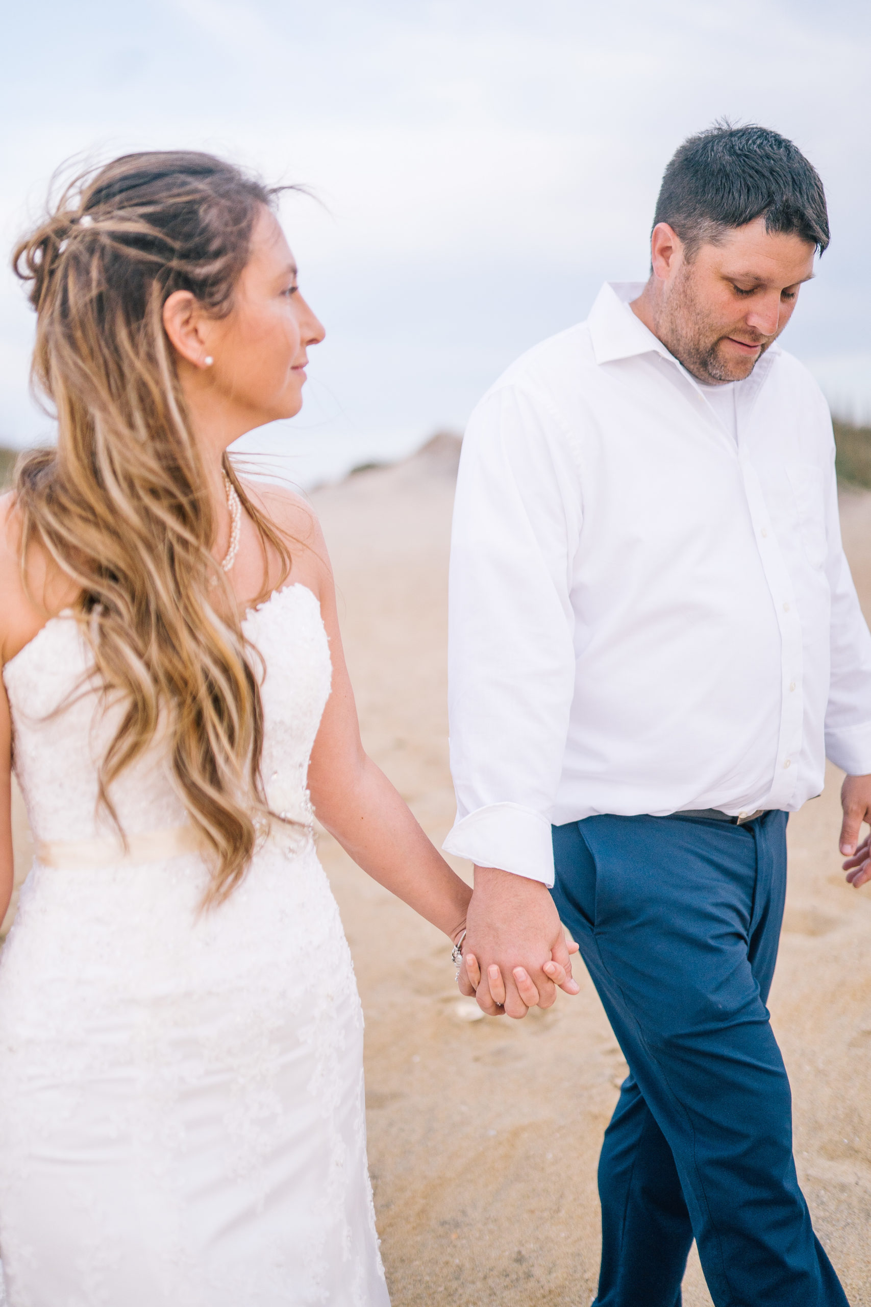 beach wedding bride and groom holding hands and walking while smiling at each other