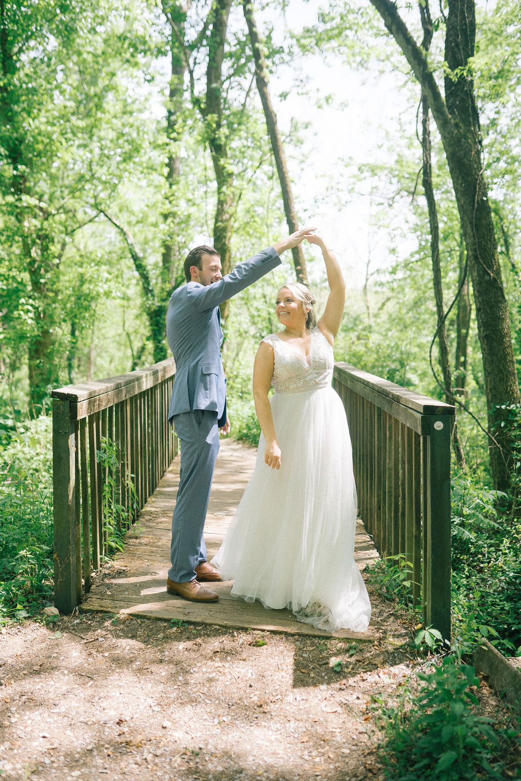 groom is wearing a blue suit and is twirling his bride on a bridge in the woods of the Ijams for their destination wedding day
