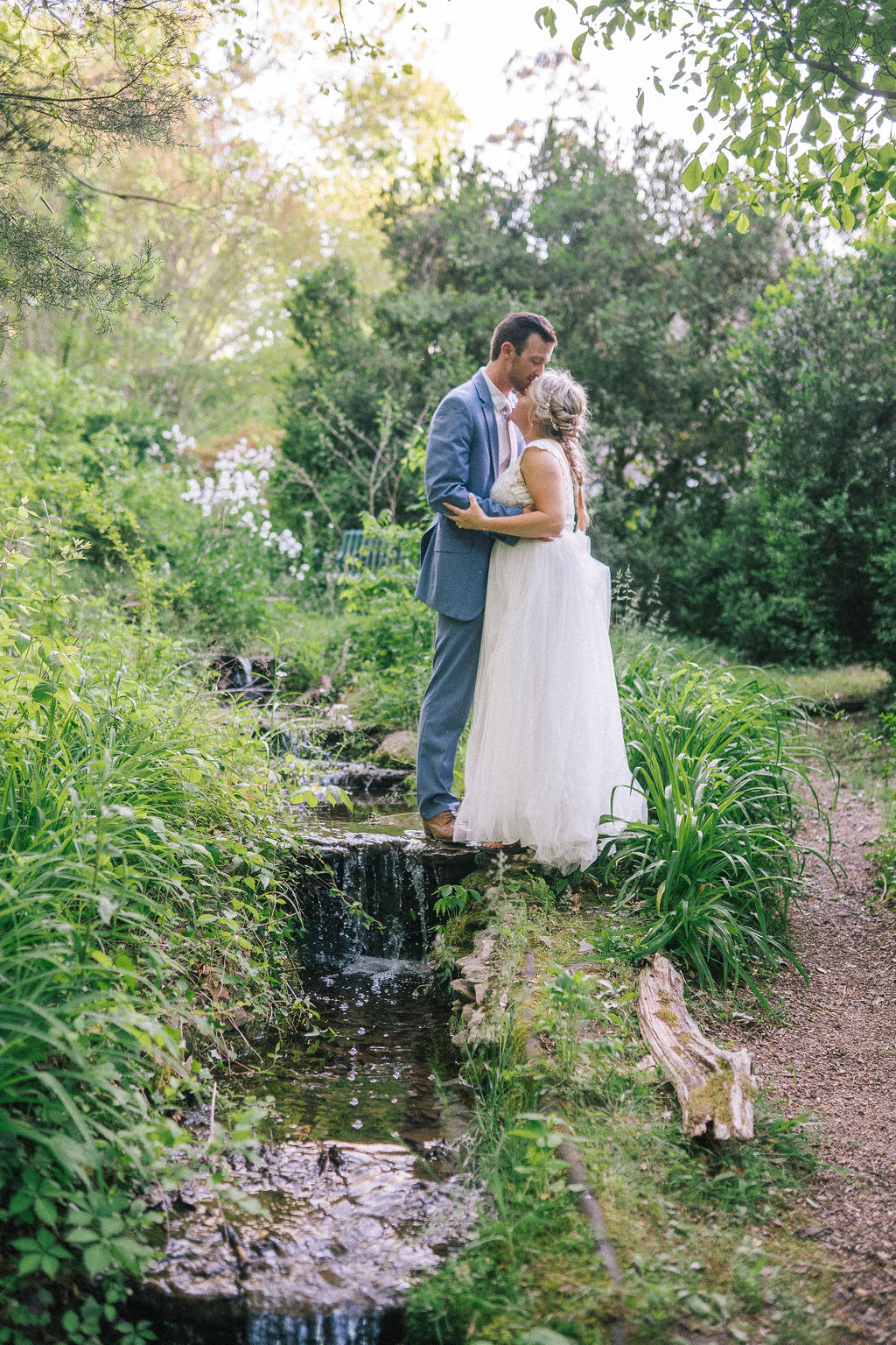bride and groom standing on a stream in the Ijams for their Tennessee destination wedding, they are kissing each other for their dream wedding day