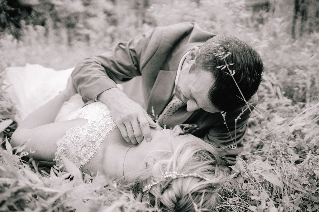 black and white photo of a bride and groom laying down on a patch of grass in the Ijams. Groom is caressing brides face
