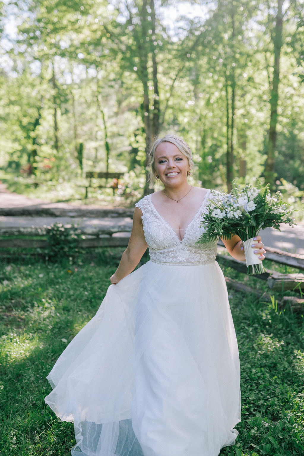 southern bride in a Vowed dress with lace detail on the bodice and a flowy skirt. Bride is in the Ijams, holding her bouquet and walking toward the camera while holding her dress